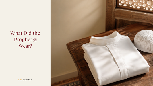 Folded white thobe and prayer cap on a wooden bench beside a cream Sunaan title panel reading What Did the Prophet Wear
